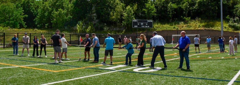 Teams of 6 stand on opposite sides of a tug-of-war rope, preparing to start the game.