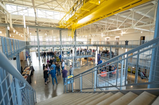 Event attendees stand around an open spaced mezzanine eating small bites and talking amongst eachother