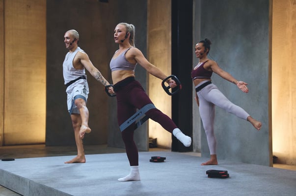 A group of people stand straight up and lift their right leg to the side.