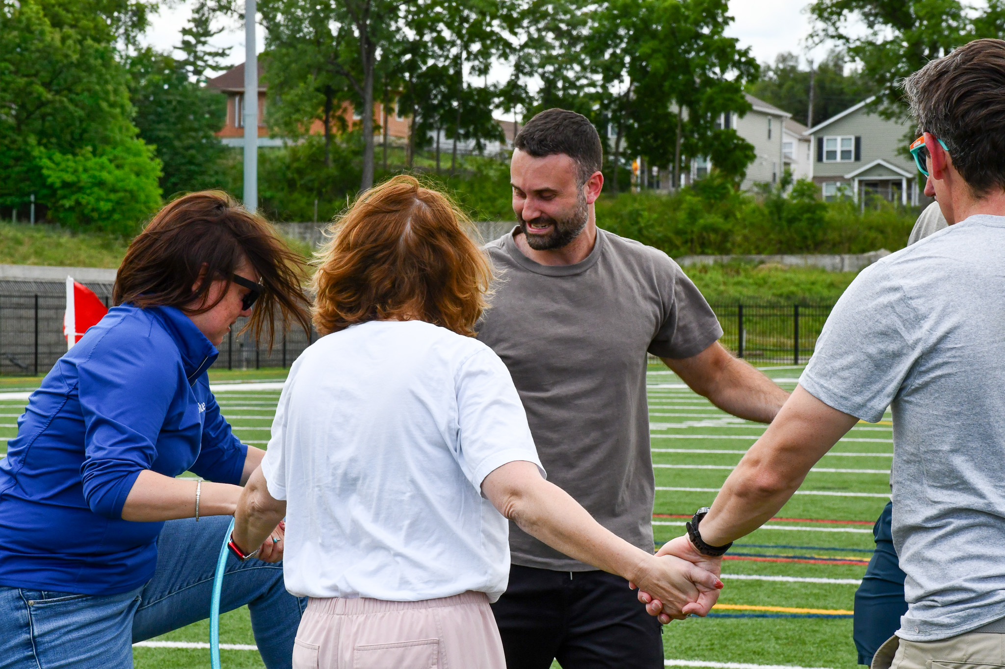 A group of four people participates in a team-building activity on a grassy field, holding hands and smiling.