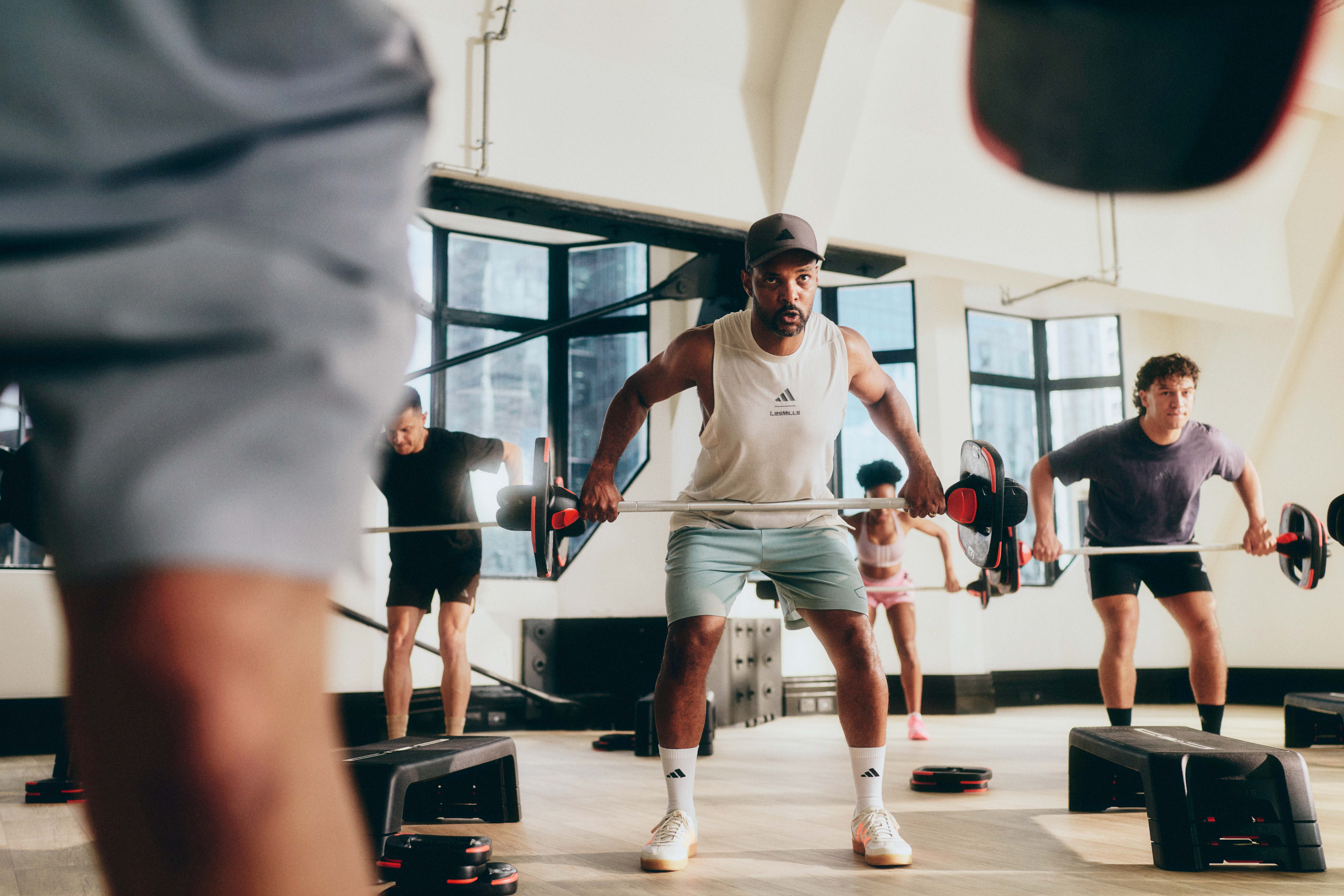 A group of people in a studio are pulling a barbell towards their chest while in a small squat.