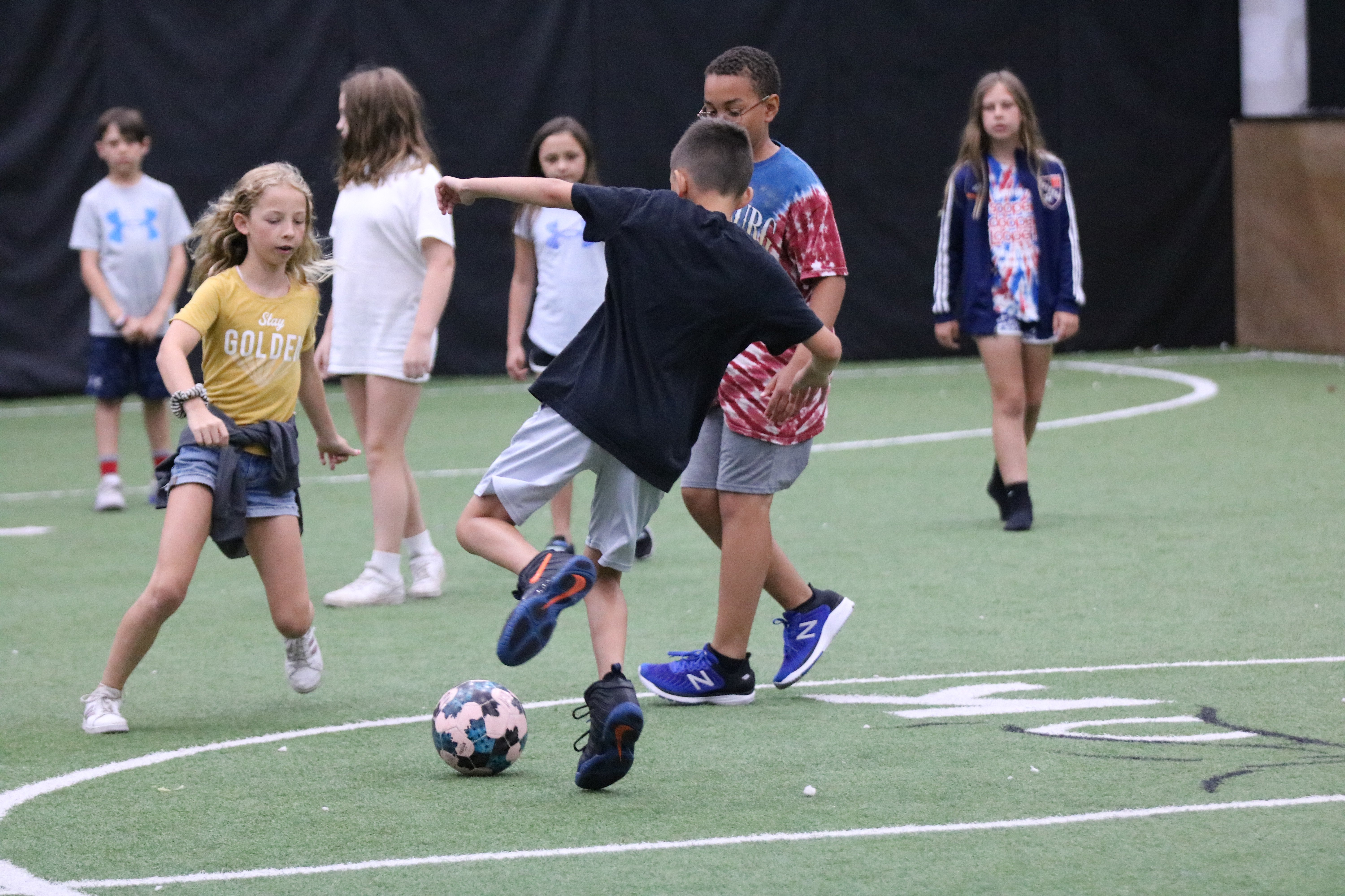 Kids running and playing soccer on a turf soccer field at a youth sports summer camp in Hamilton, Ohio